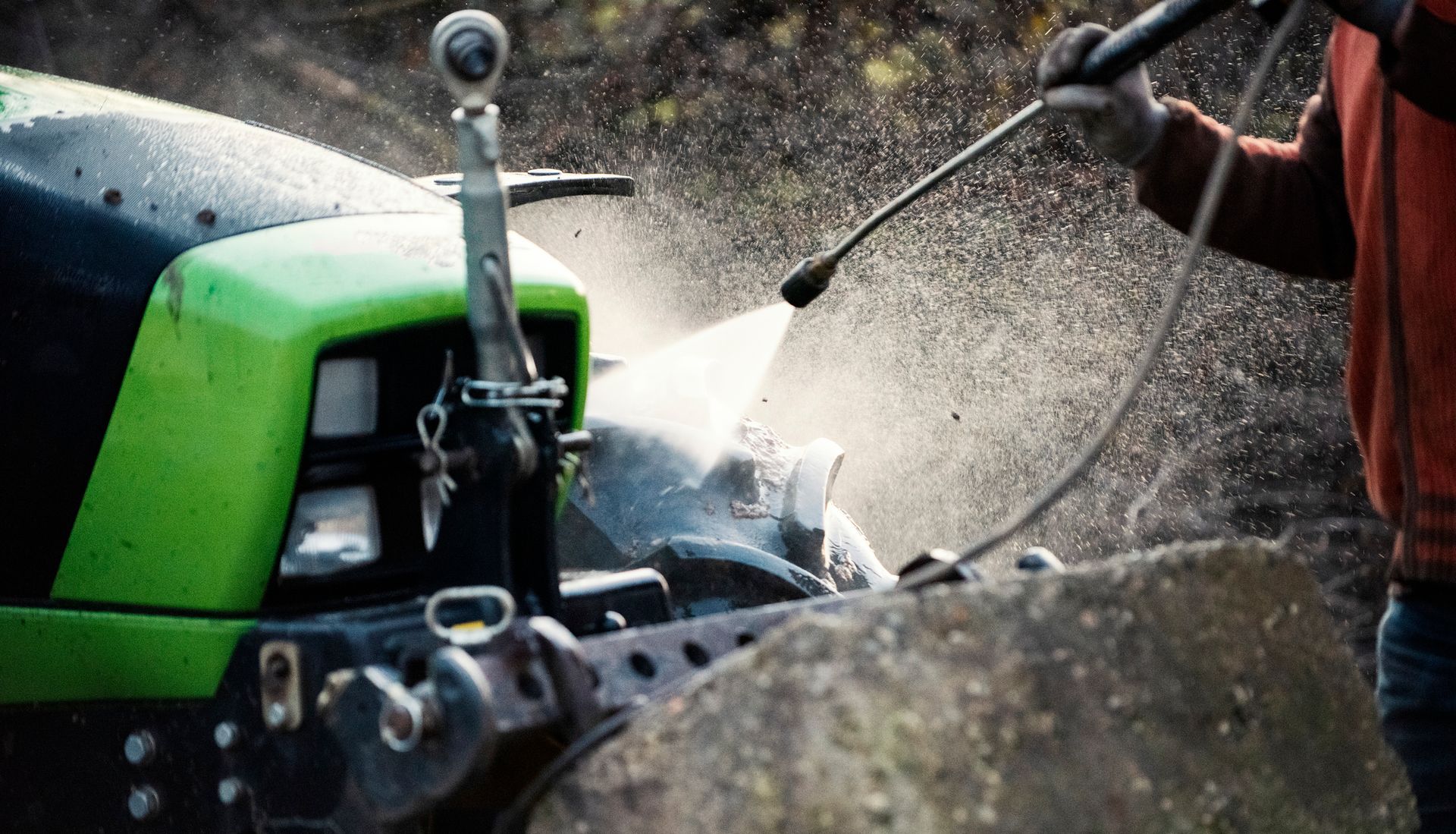 Person washing a green and black tractor with a pressure washer.