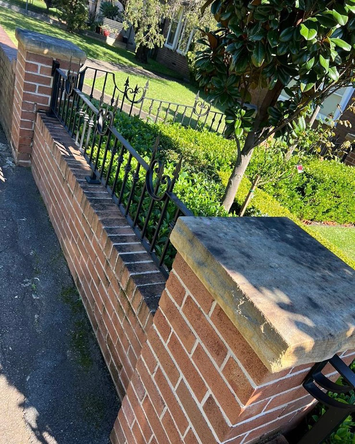 Brick wall with black metal railing, topped with stone caps, in a yard.