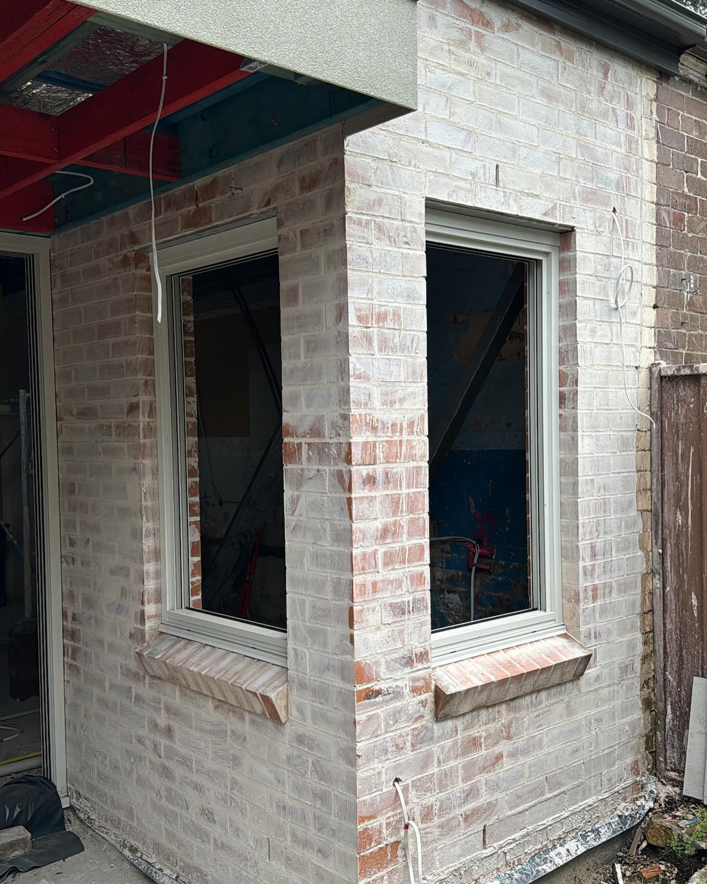 Exterior brick wall with two windows and white trim under construction.