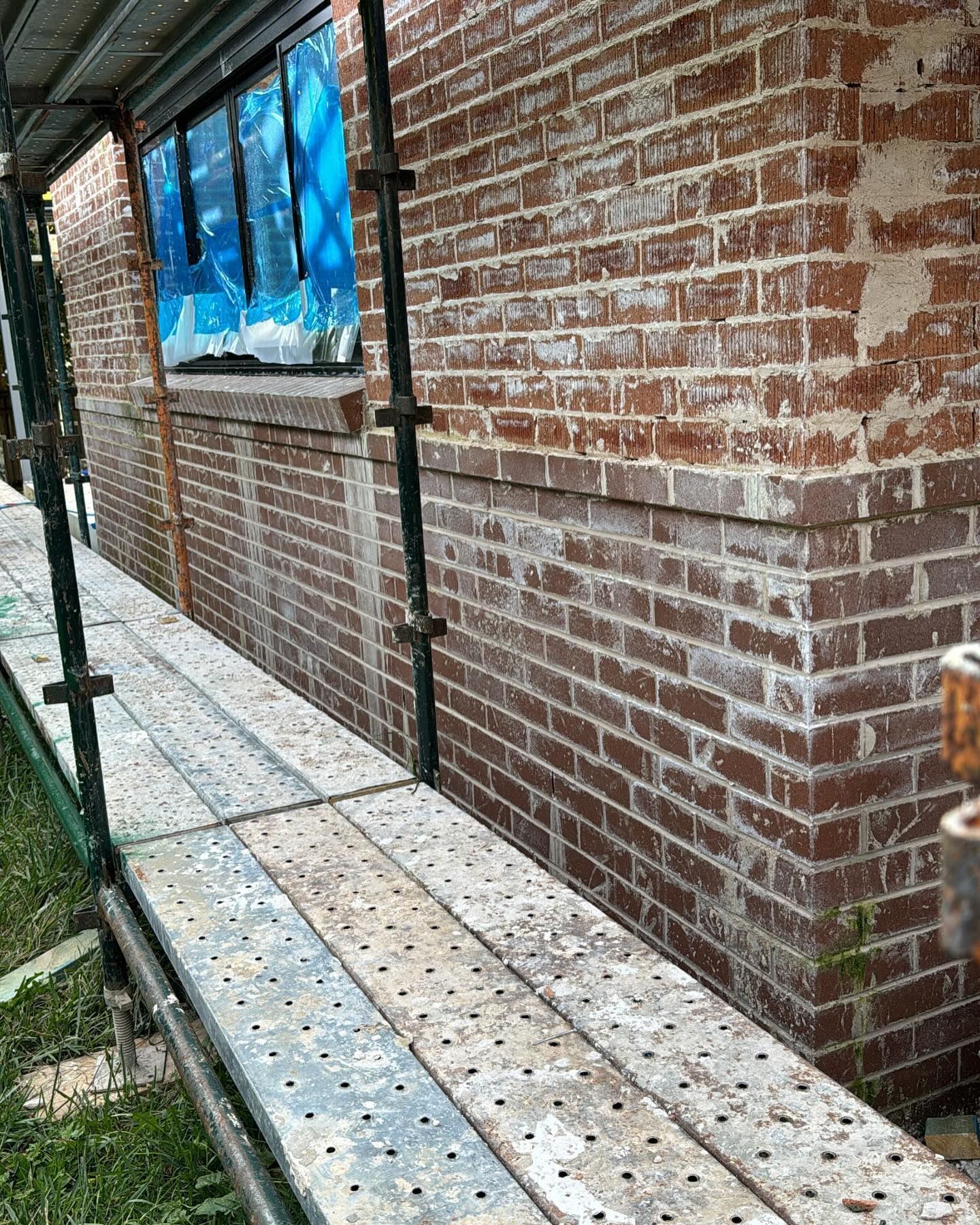 Brick building with scaffolding; window covered in blue plastic.