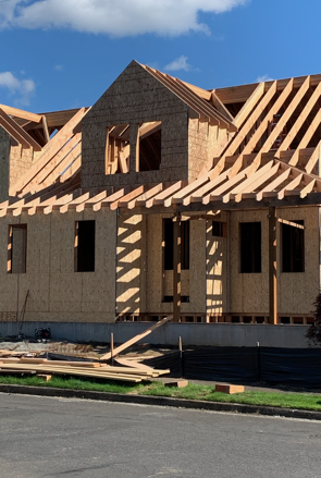 A man is standing on top of a wooden house under construction.