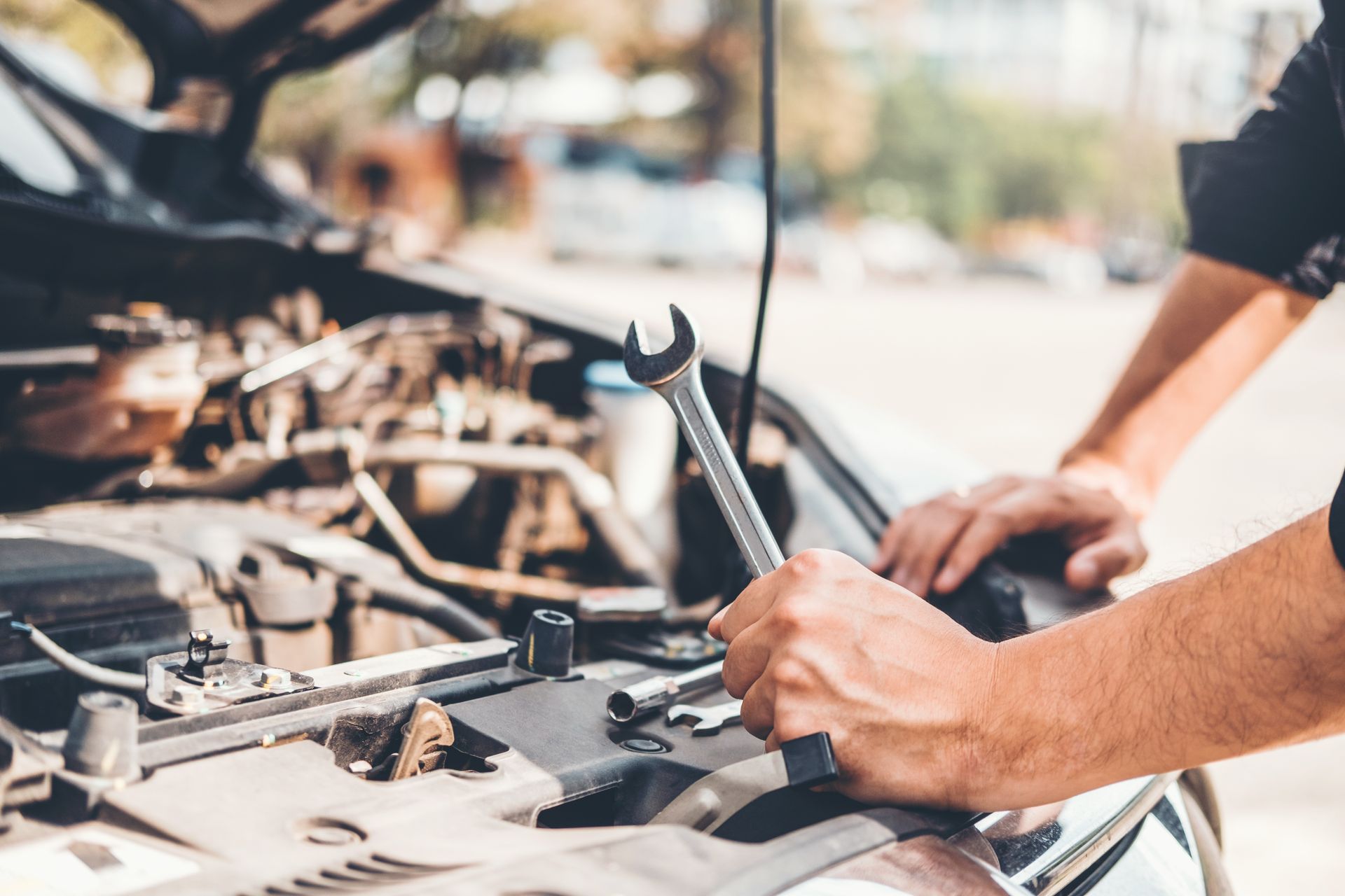 Mechanic holding a wrench while inspecting and working under the hood of a car.