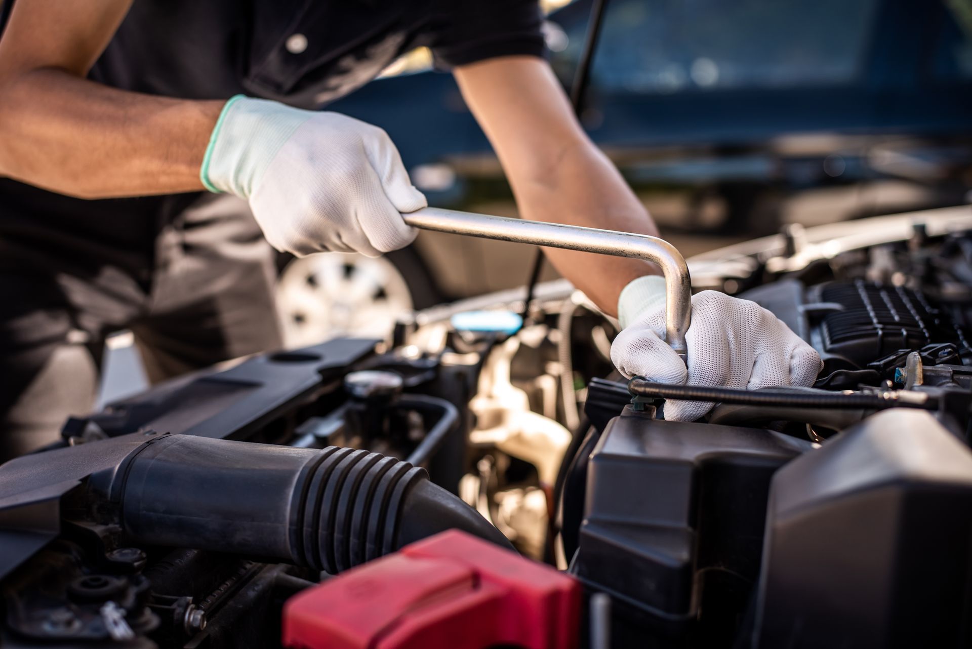 Gloved mechanic using a wrench to service a car engine under an open hood