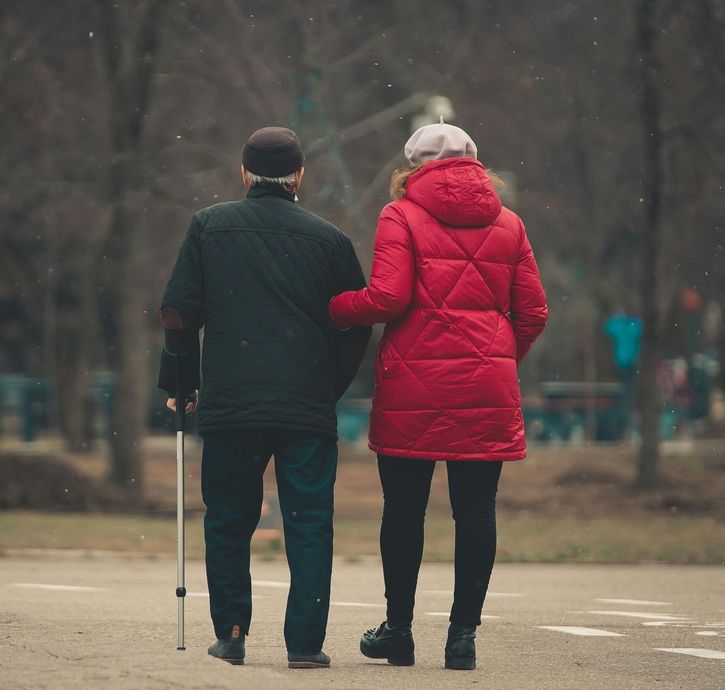 A man with a cane and a woman in a red coat are walking down a street