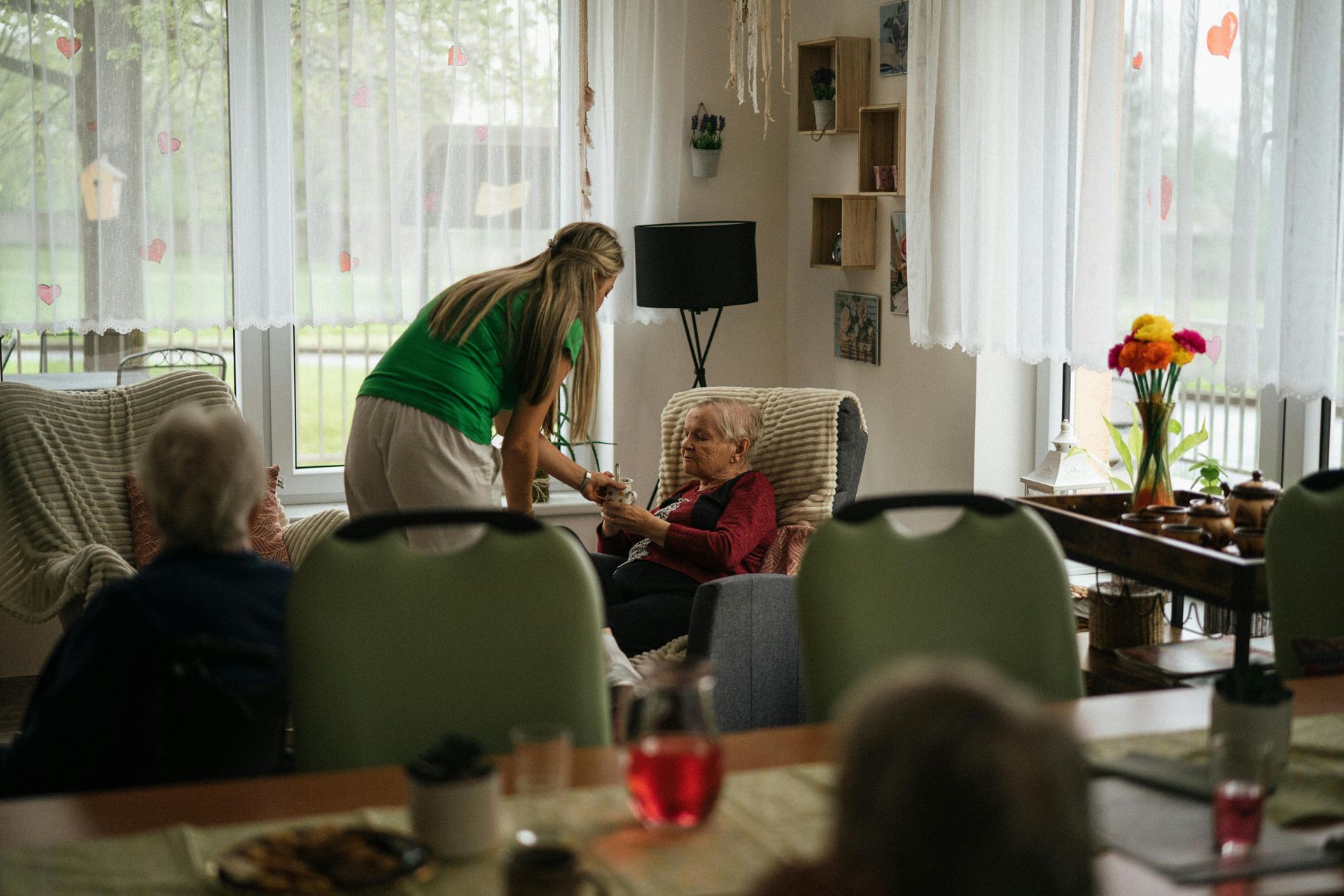 A woman is standing next to a man in a chair in a living room.