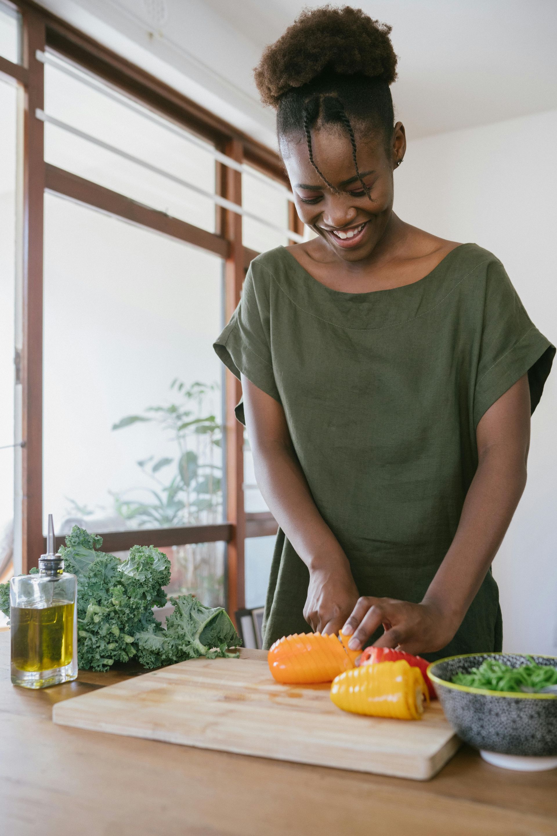 A woman is smiling while cutting peppers on a cutting board.