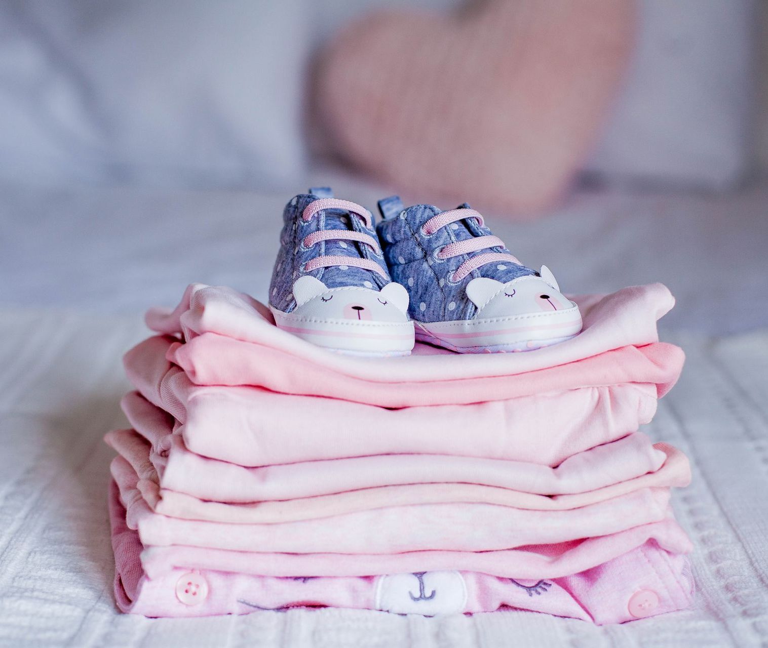 A pair of baby shoes are sitting on top of a pile of pink clothes.