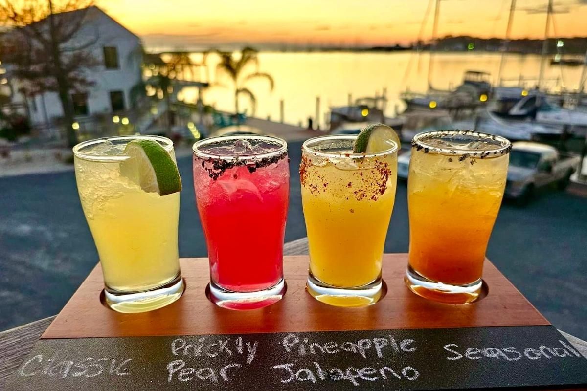 Cocktails on serving tray with harbor and boats at sunset in background on an autumn evening