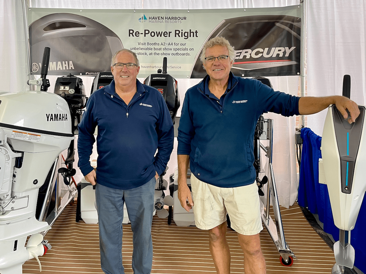 Two employees pictured at boat show booth with outboard motors on display