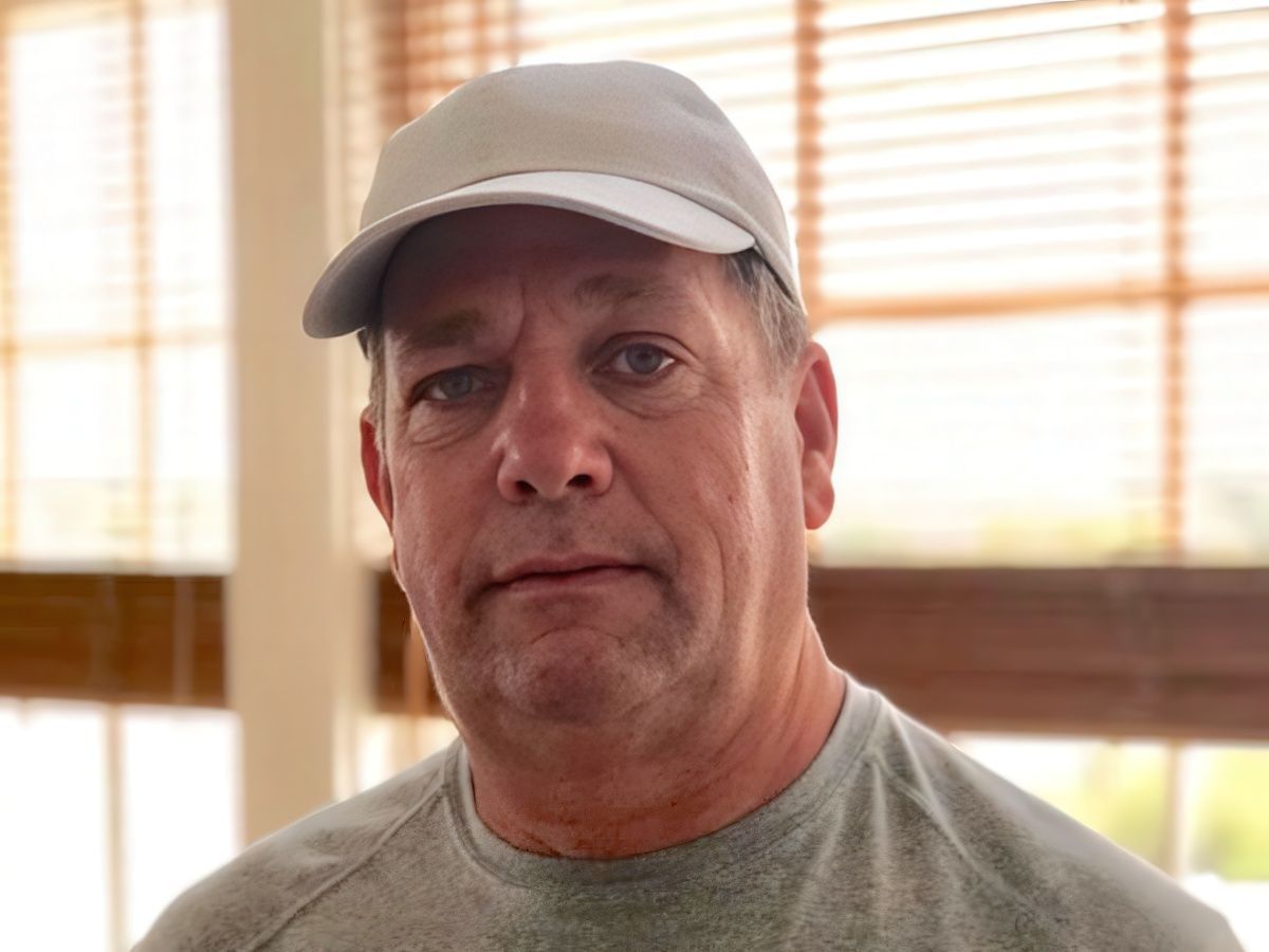Man posing for photo wearing gray shirt in front of blinds on window in background