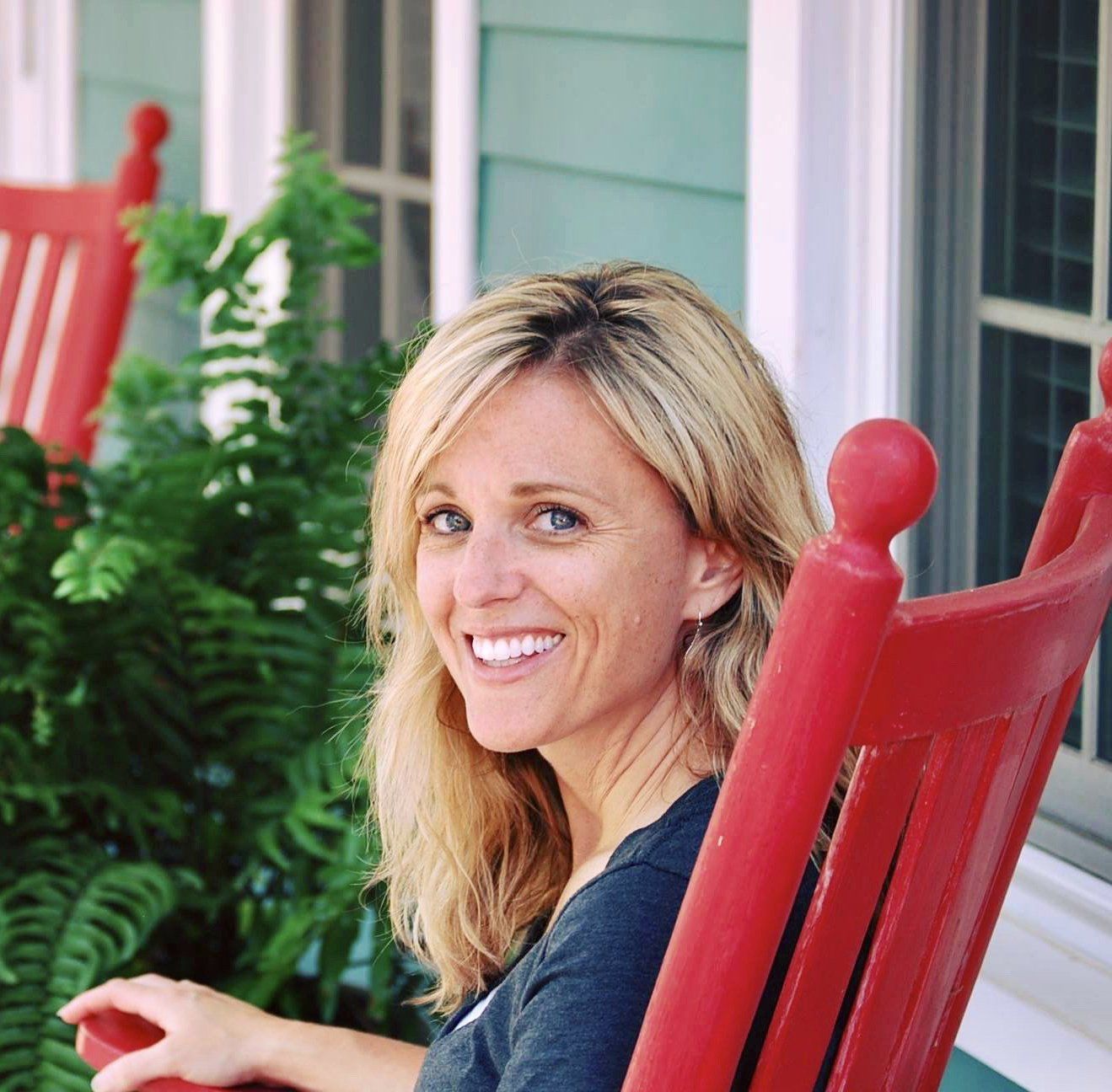 Woman seated in rocking chair outside with plants and windows in the background