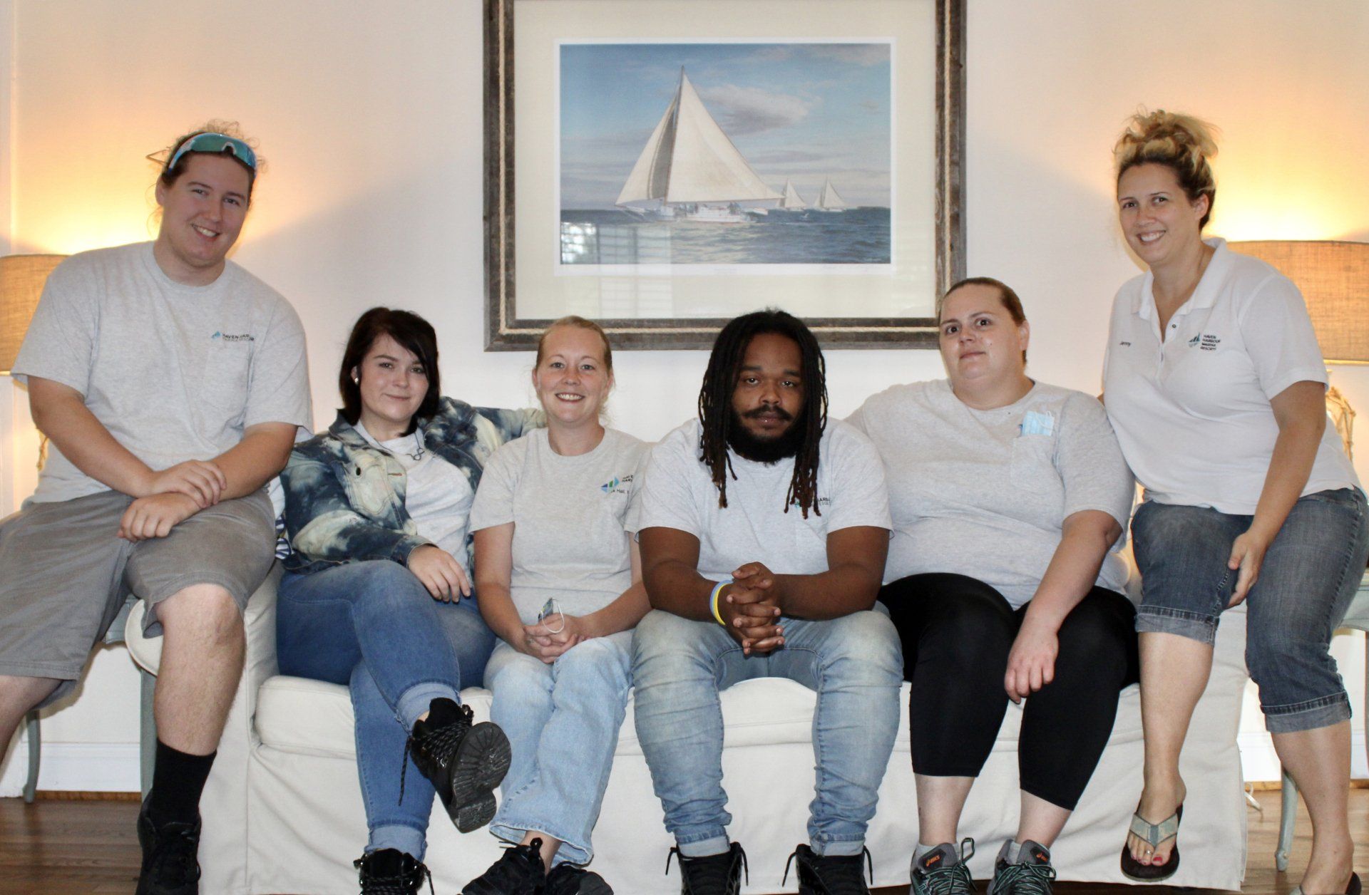 Employees pose for a group photo on a sofa under painting of sailboat
