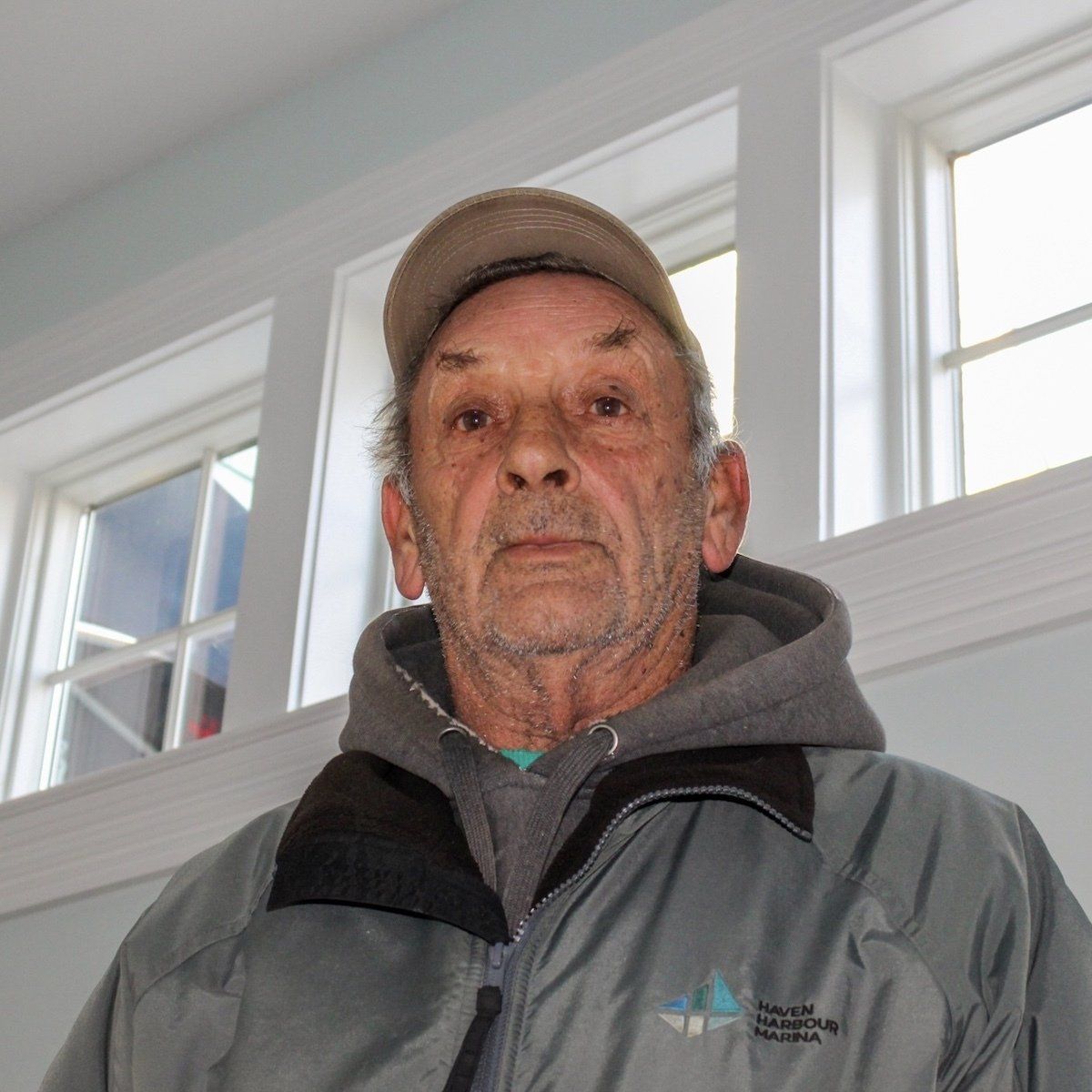 Older male employee pictured indoors in front of window wearing a jacket