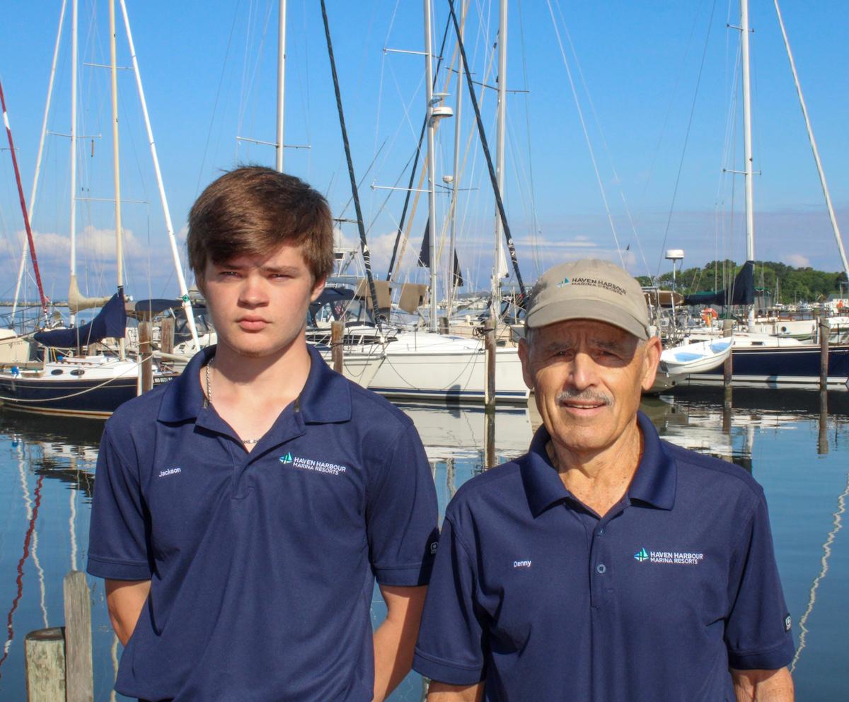 Two employees pictured outside in front of sailboats