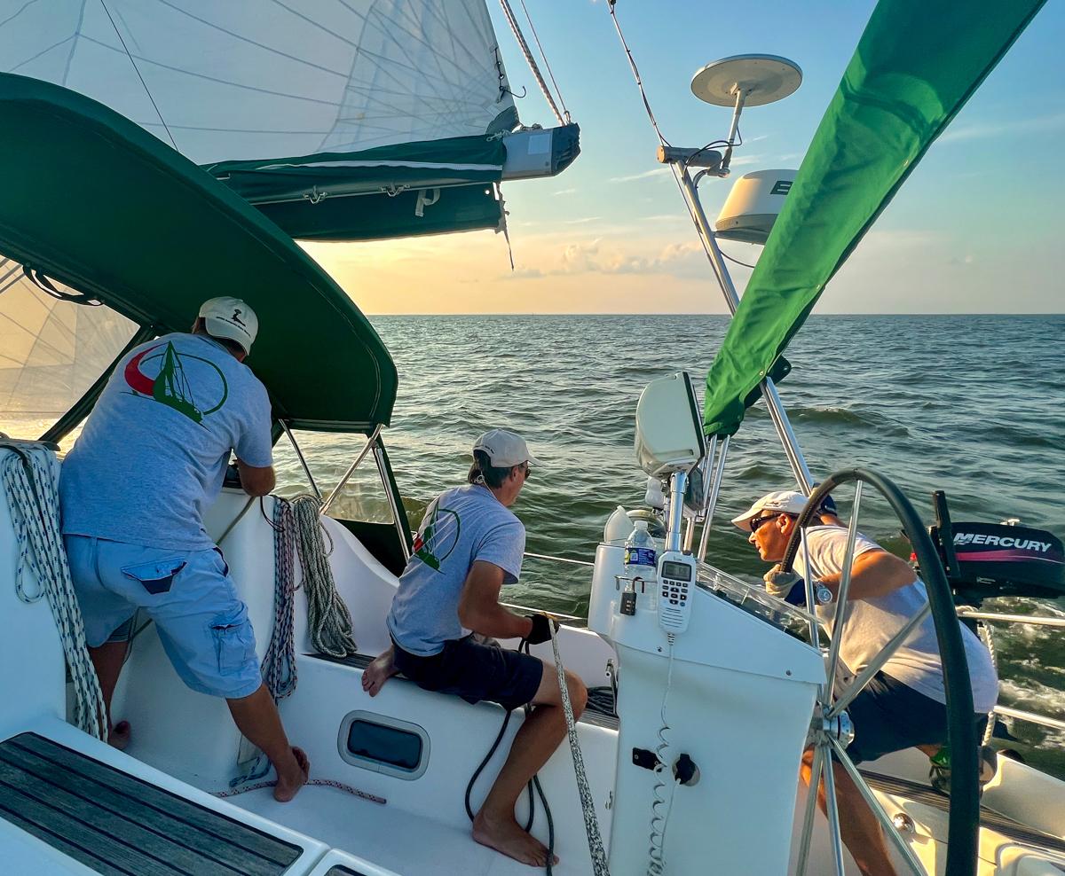 Sailboat crew of three men adjust lines and steering