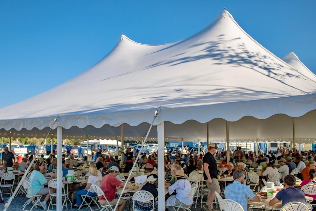 People seated under outdoor tent on sunny day eating and talking