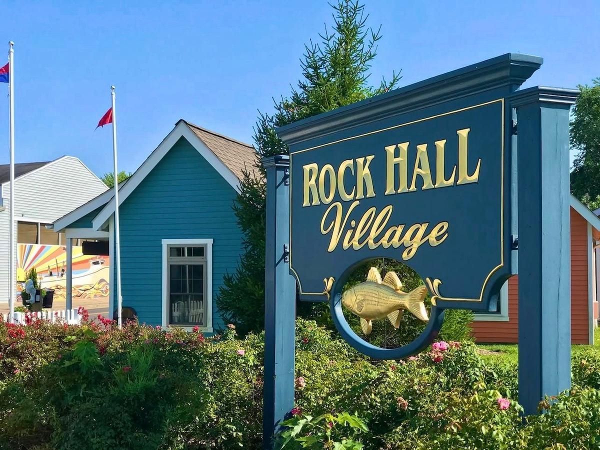 Sign for Rock Hall Village, with blue and orange buildings in the background