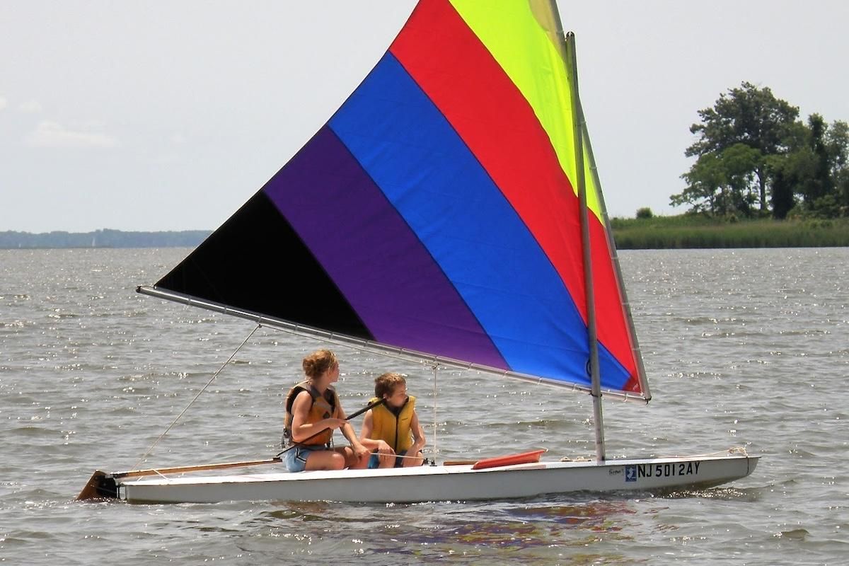 Two youth pictured sailing a small craft on open water on an overcast summer day.