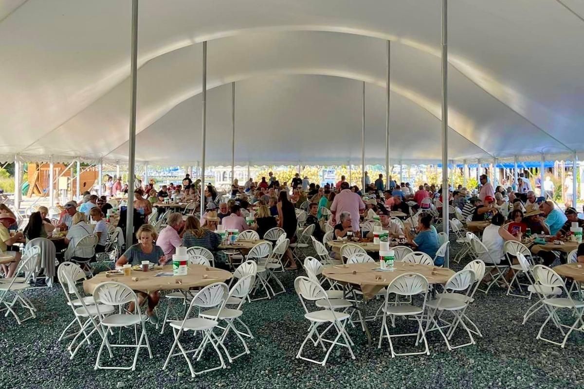 People seated under outdoor tent on sunny day eating and talking