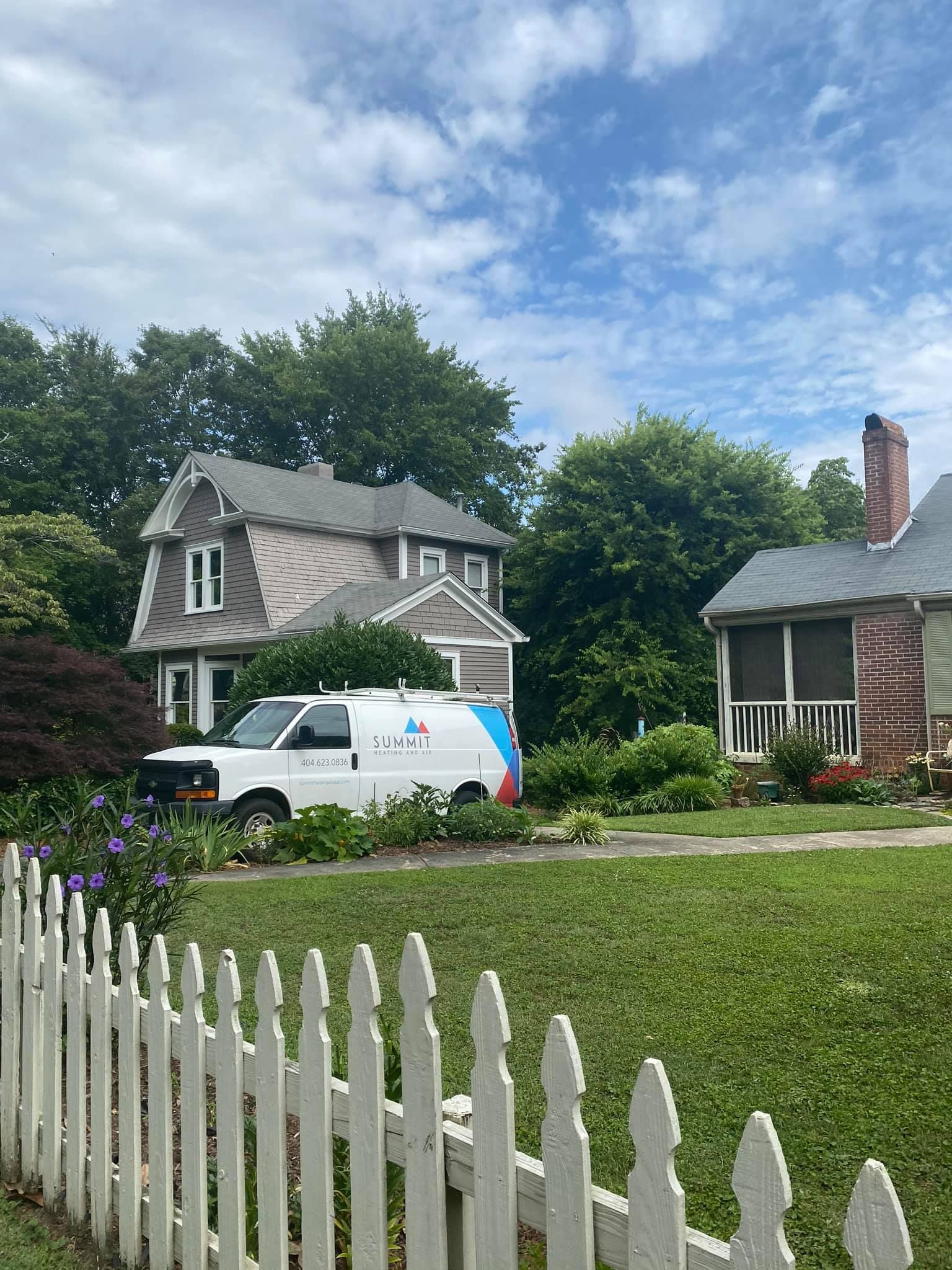 A white van is parked in front of a house with a white picket fence.