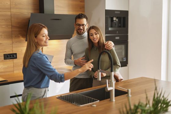 A woman is talking to a man and woman in a kitchen.