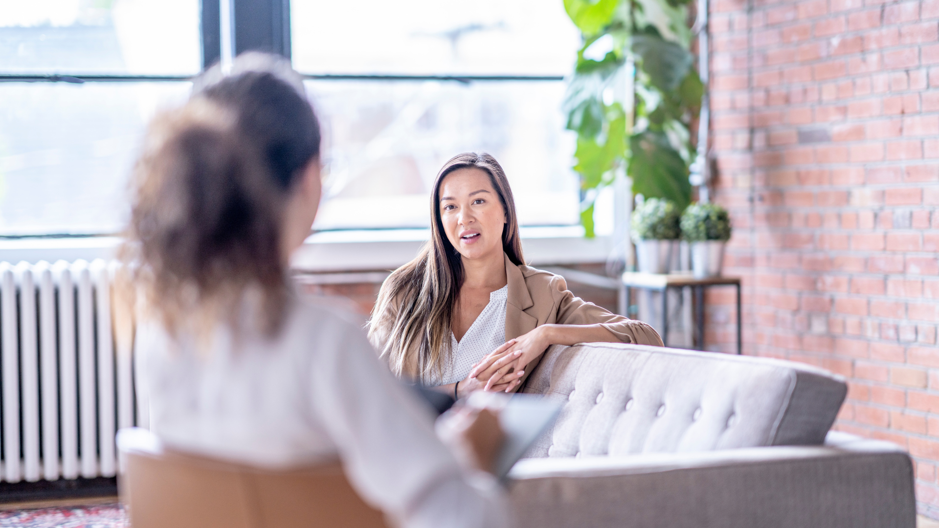 Woman in a blazer and another person in an office setting, having a conversation.