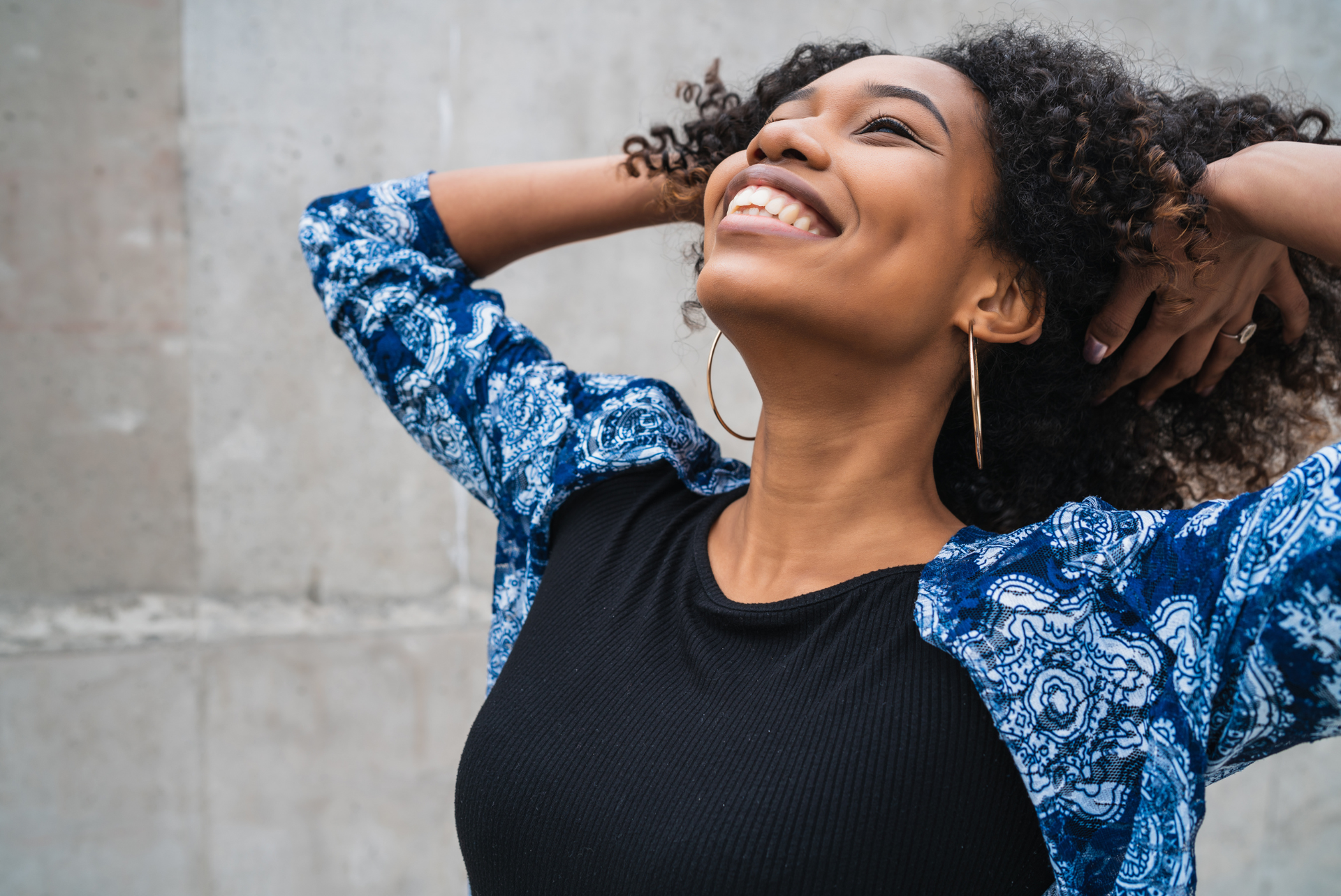 Woman with curly hair smiles, arms raised, looking up