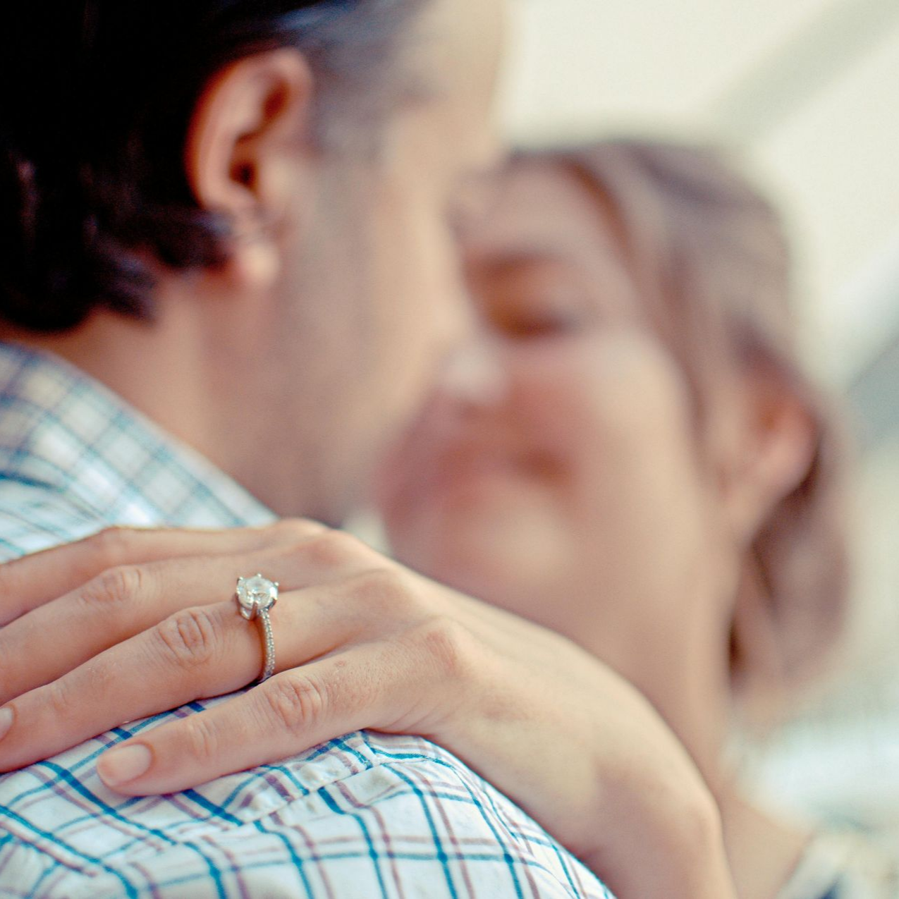 Man embraces woman, engagement ring on her finger, focus on ring.