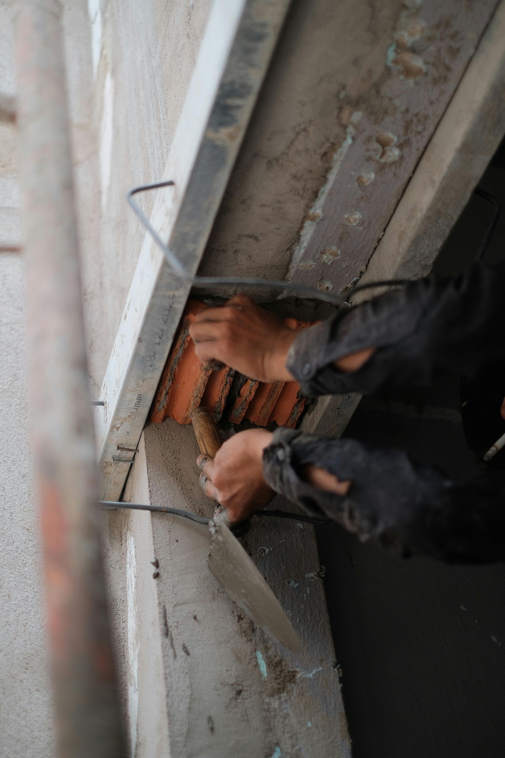 Person in black sleeves working on a construction site, using a tool to adjust the orange tiles.