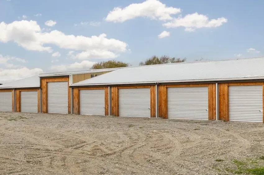 Storage units with white doors and brown wood trim under a blue sky.