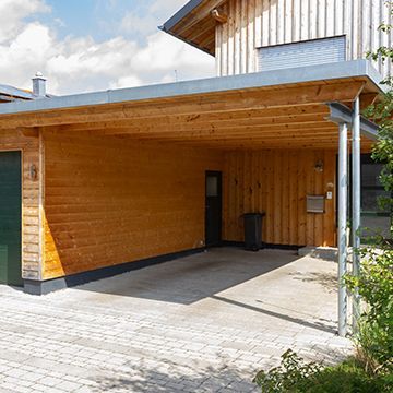 A wooden garage with a green door is next to a house