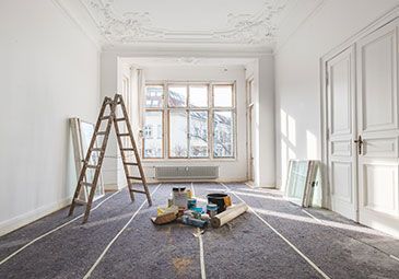 An empty room with a ladder and paint supplies on the floor.