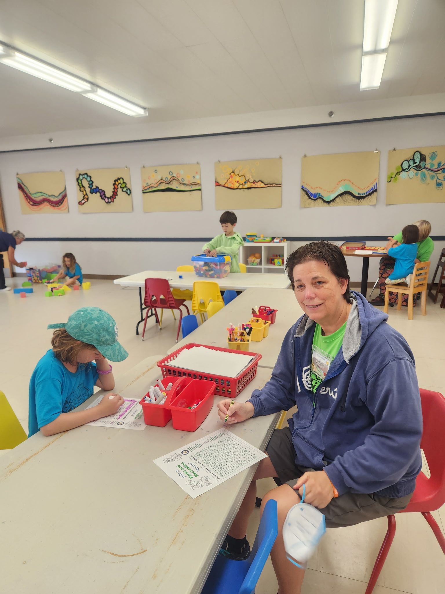 A woman is sitting at a table in a room with children.