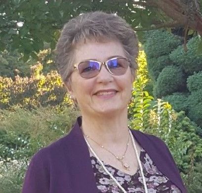 A woman wearing sunglasses and a purple jacket is smiling for the camera.