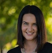 A white woman with shoulder length brown hair is smiling for the camera while wearing a black shirt and a necklace.
