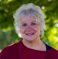 A woman with white hair and a red shirt is smiling for the camera.