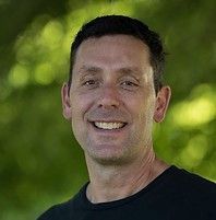 A man in a black shirt is smiling for the camera.