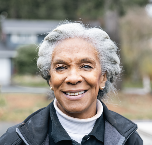A Black woman with gray hair is smiling and wearing a black jacket.