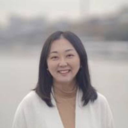 An Asian woman in a white jacket is smiling for the camera.