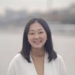 An Asian woman in a white jacket is smiling for the camera.
