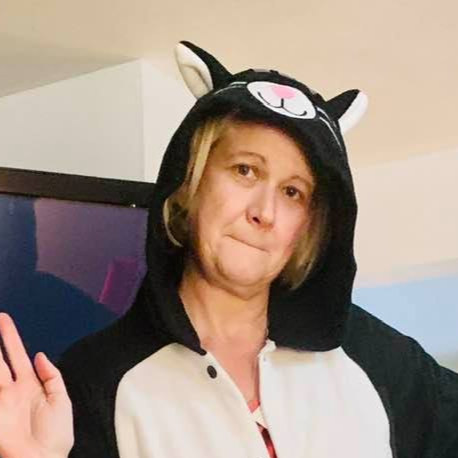 A blond woman with purple stripe in her hair and a tattoo on her arm is giving a thumbs up.