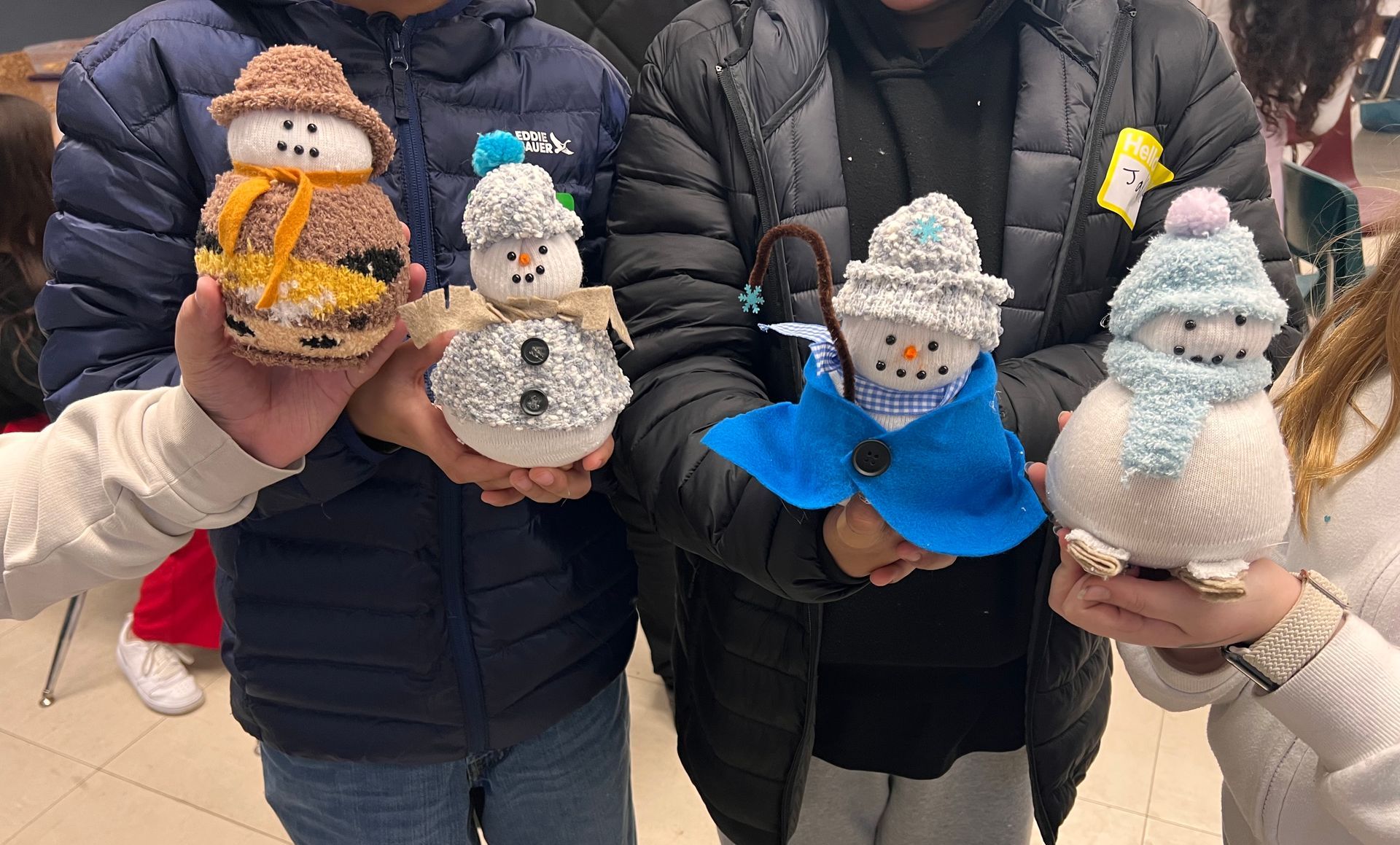 A group of people are holding knitted snowmen in their hands.