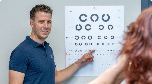 A man is pointing at a chart on a wall while a woman looks at it.