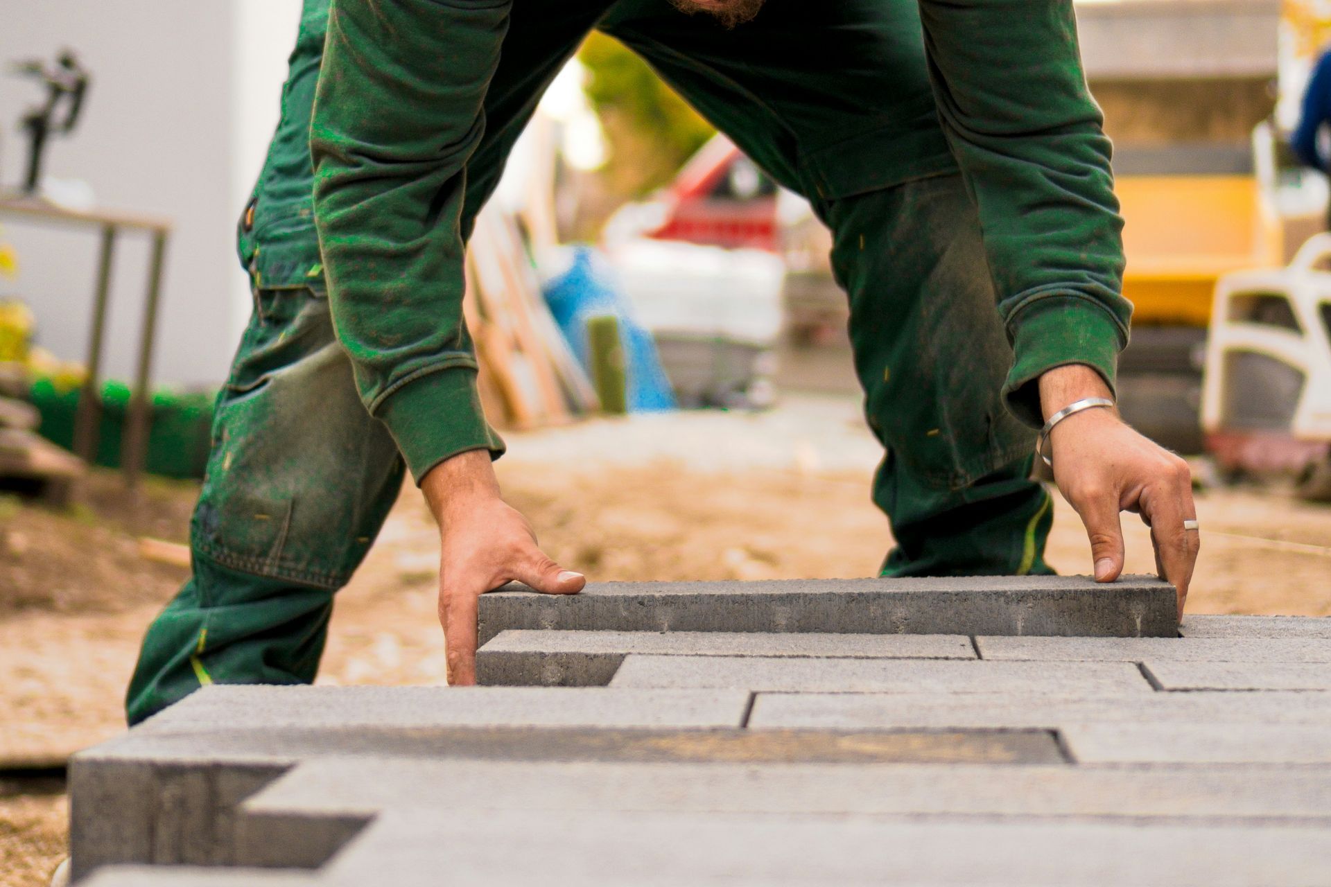 A worker in green work clothes laying gray rectangular paving stones on a construction site.