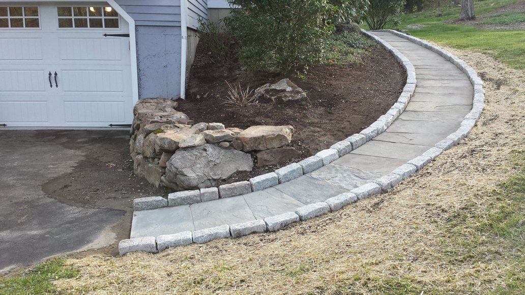A concrete walkway leading to a garage next to a house.