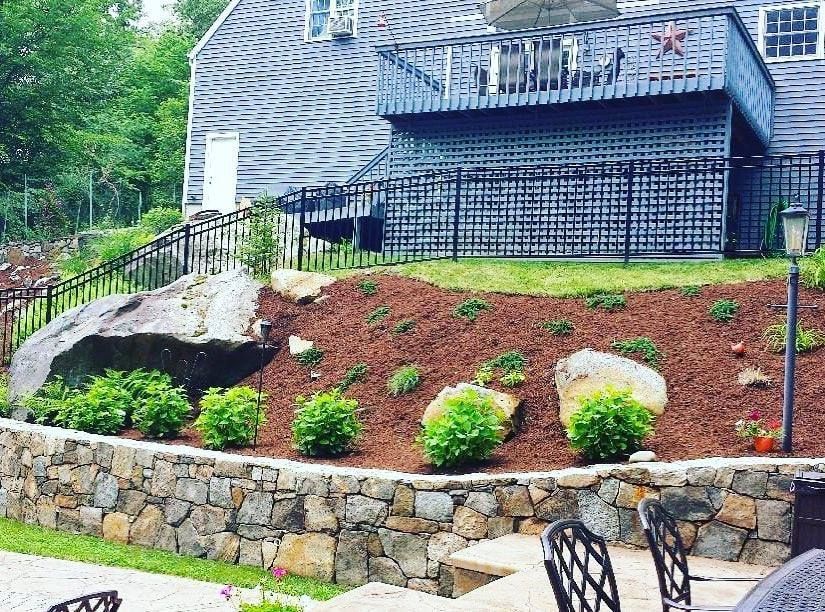 A stone wall surrounds a patio area in front of a house.