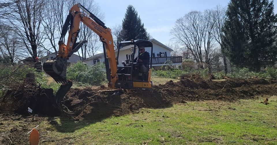 A yellow excavator is digging a hole in a grassy field.
