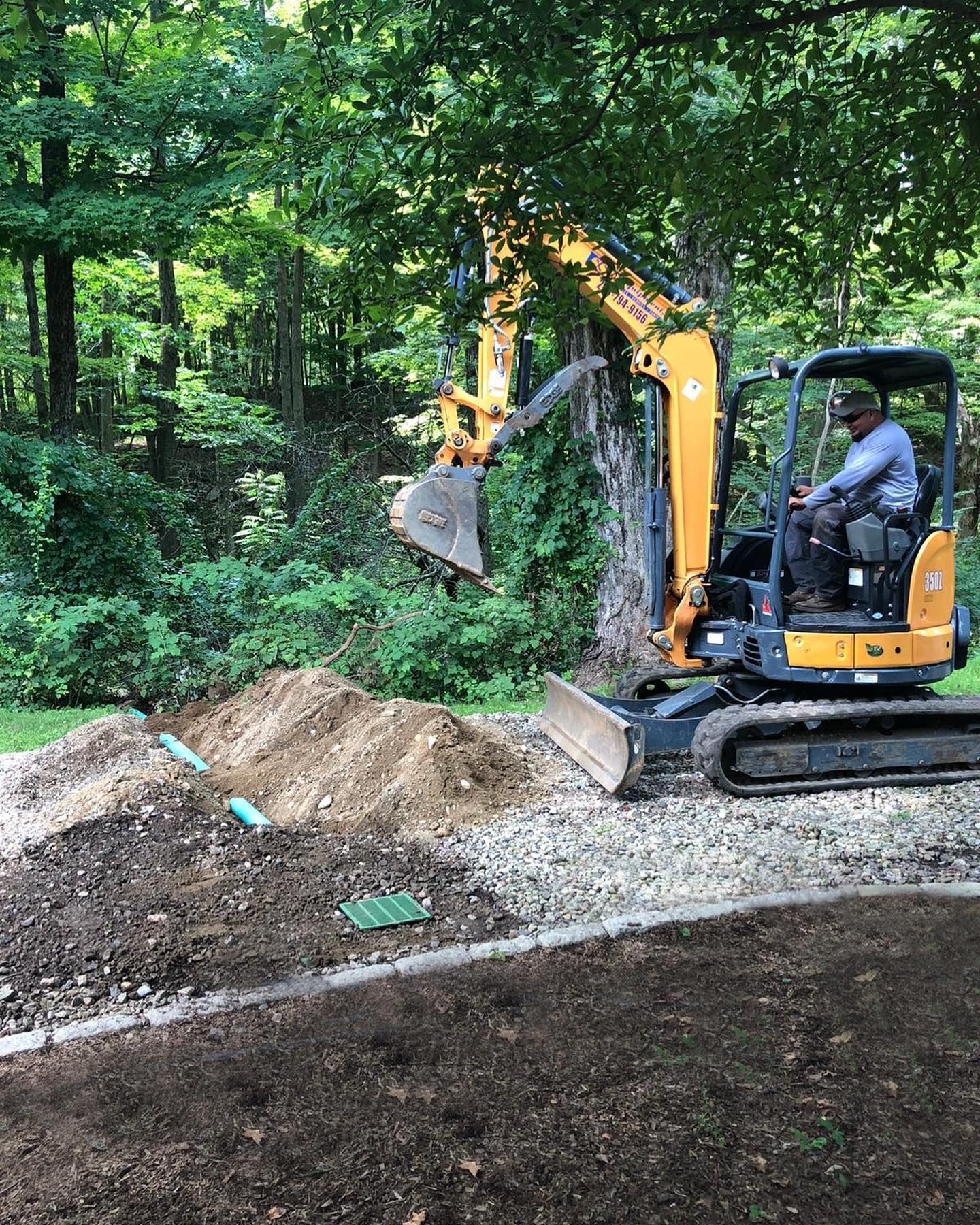 A man is driving a small excavator on a dirt road.