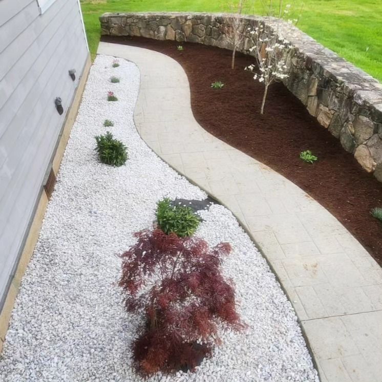 A walkway surrounded by gravel and plants with a stone wall in the background