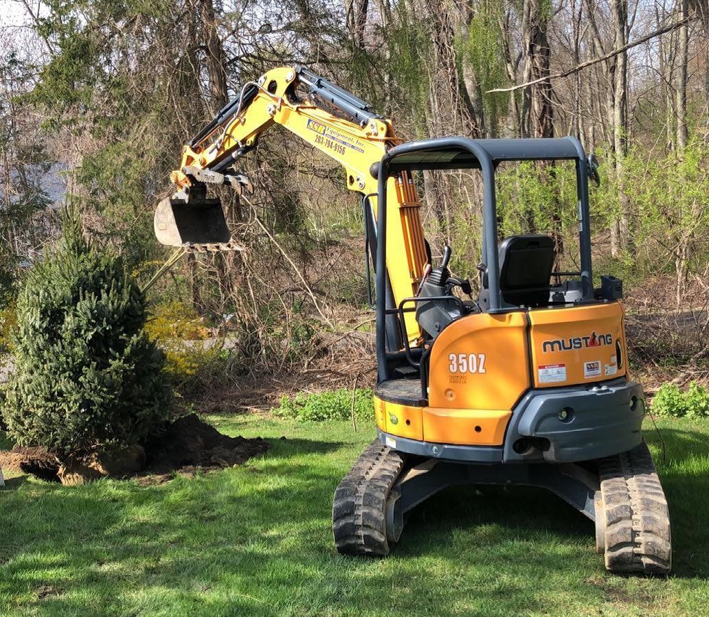 A small yellow excavator is sitting in the grass in a yard.